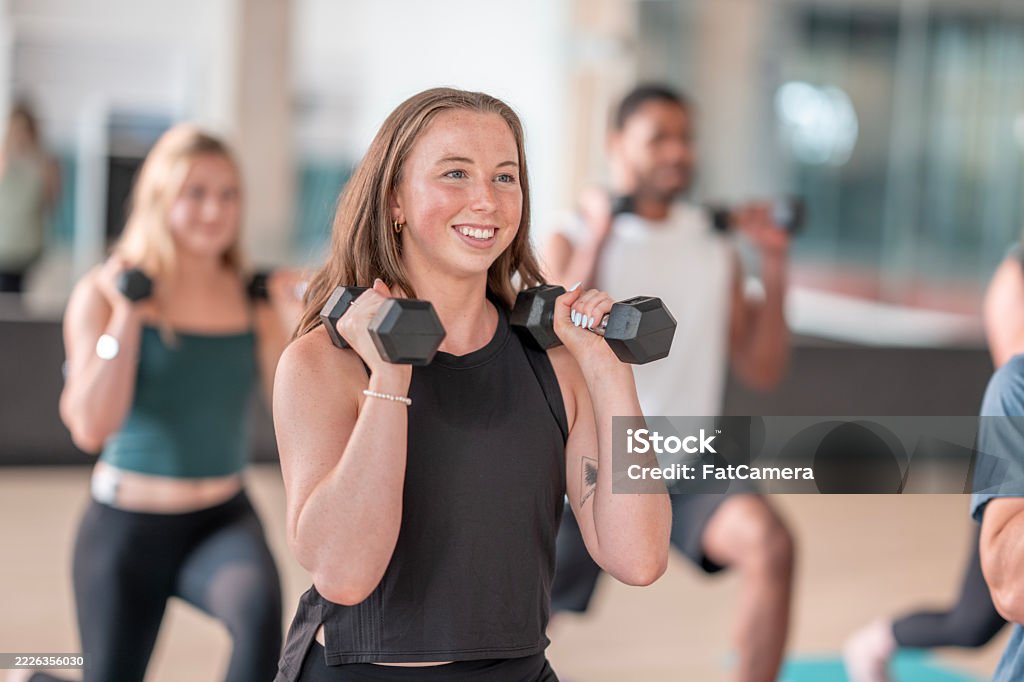 Two girls and 1 man are lifting dumbbells in gym.